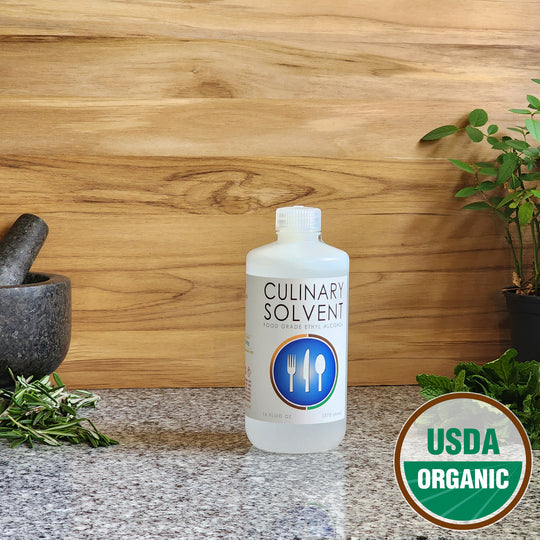 Pure USDA Organic Food Grade Ethanol pint bottle by Culinary Solvent with rosemary, mint, and fresh herbs for tincture on teak wood background