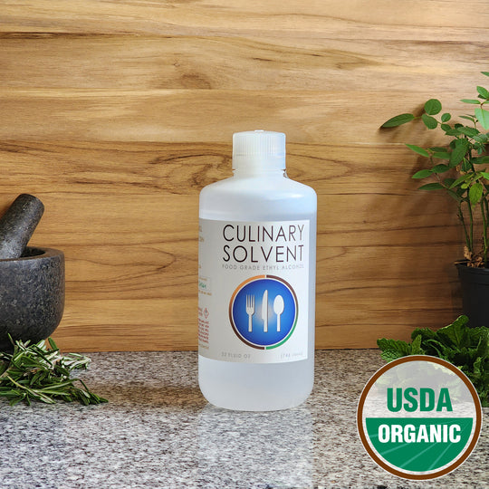 Pure USDA Organic Food Grade Ethanol quart bottle by Culinary Solvent with rosemary, mint, and fresh herbs for tincture on teak wood background