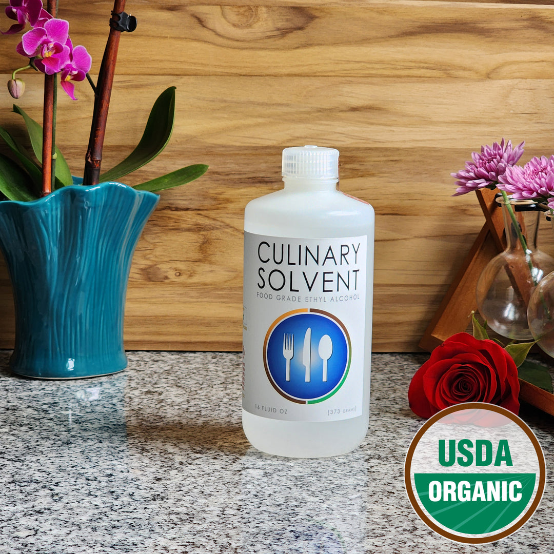 Pure Organic Perfumers Alcohol pint bottle by Culinary Solvent food grade ethanol with orchids, roses, and fresh flowers teak wood background