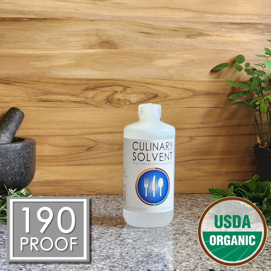 Pure USDA Organic Food Grade Ethanol pint bottle by Culinary Solvent with rosemary, mint, and fresh herbs for tincture on teak wood background