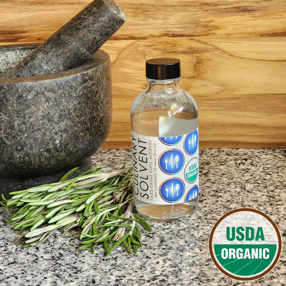 Pure USDA Organic Food Grade Ethanol glass bottle by Culinary Solvent with rosemary, mint, and fresh herbs for tincture on teak wood background