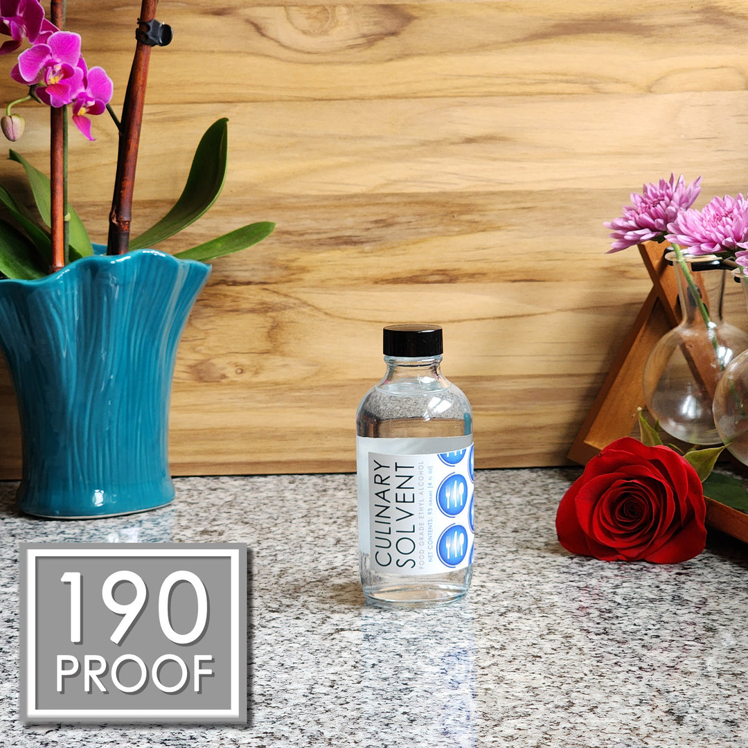 Pure Perfumers Alcohol glass bottle by Culinary Solvent food grade ethanol with orchids, roses, and fresh flowers teak wood background