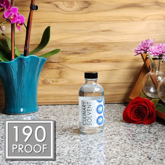 Pure Perfumers Alcohol glass bottle by Culinary Solvent food grade ethanol with orchids, roses, and fresh flowers teak wood background
